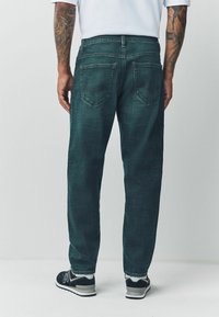 Tumedrohelised denimiteksad lõdva lõikega, millel on kaks tagataskut ja tuhmunud tekstuur. Kanditud koos mustade spordijalatsitega.