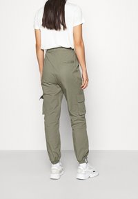 Olivgröna cargobyxor med avsmalnande anklar, flera sidofickor och en åtsittande midja, matchade med en vit t-shirt och vita sneakers.