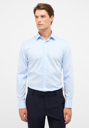 Chemise bleu clair à manches longues avec un col étalé, fermeture par boutons et manches à poignets, associée à un pantalon sombre. Texture de tissu lisse.