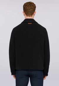 Svart ulljacka med krage, med en bakre läderetikett och knappade ärmslut. Designad med en strukturerad silhuett och slät textur.