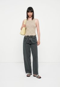 Beige strikket tank topp med mønster, høyt liv mørkegrå vide bukser, og svarte og hvite slangeskinnsandaler. Gul skulderveske.