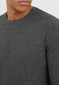 Dunkelgrauer Rundhals-Pullover aus strukturiertem Stoff. Das Material wirkt weich mit einem dezenten, gleichmäßig verteilten Muster.