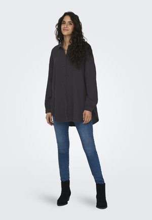 Dark gray long-sleeve button-up shirt with a straight cut, rounded hem, and soft texture, paired with blue skinny jeans and black ankle boots.