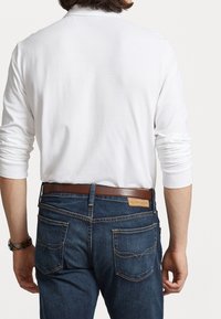 Bílá košile s dlouhým rukávem v kombinaci s tmavě modrými džíny. Džíny mají dvě zadní kapsy s šitím a doplňuje je hnědý kožený pásek.