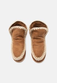 Pantofole in pelle marrone con un interno morbido, caratterizzate da una trama intrecciata crema attorno all'apertura e una suola piatta.