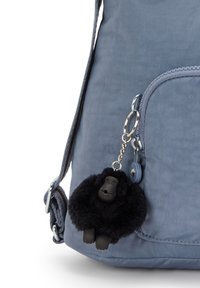 Sininen kangaskassi, jossa on sileä pinta ja säädettävä olkahihna, sekä musta karvainen gorilla-avainketju kiinnitettynä.