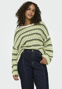 Lahki pleten jacket s zelenimi in belimi zig-zag črtami, širokimi rokavi in čolnasto izrezano ovratnikom. Ujemajoče se z temno denim kavbojkami.