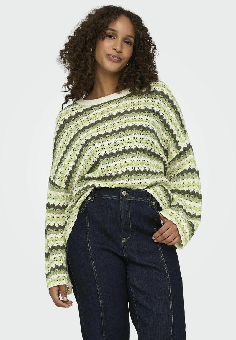 Lahki pleten jacket s zelenimi in belimi zig-zag črtami, širokimi rokavi in čolnasto izrezano ovratnikom. Ujemajoče se z temno denim kavbojkami.