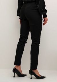 Pantalon noir ajusté à la coupe slim avec une texture lisse, doté de poches arrière. Associé à des talons noirs avec un bout métallique.