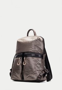 Mochila de nylon gris con una forma estructurada, doble cremallera frontal, correas negras texturizadas y un sutil detalle de marca en las correas.