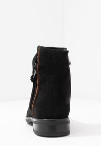 Bottine en daim noir avec une finition lisse et texturée, dotée d'une fermeture éclair latérale et d'accents marron contrastants le long de la couture. Semelle en caoutchouc.