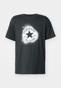 Juodas medvilnės marškinėliai, turintys baltą apvalią grafiką su žvaigžde, tekstais "CONVERSE" ir "Chuck Taylor" šiuolaikiniu šriftu, trumpomis rankovėmis.