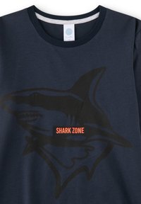 Dunkelblaues T-Shirt mit großem schwarzem Haifisch-Print und hellorangefarbenem Text "SHARK ZONE" in der Mitte. Weiches Baumwollmaterial.