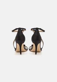 Black satin high-heeled sandals with an open back, adjustable ankle strap, and slender heel. Smooth texture with minimalist design.
