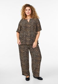 Leopardmönstrad topp med avslappnad passform och vida byxor i bruna och svarta nyanser, med korta ärmar och detalj med nyckelhål i halsen. Svarta skor.