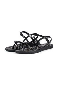 Schwarze Sandalen mit flexiblen Kreuzriemen, einer Schnallenverschluss, flacher Sohle und einem gemusterten Fußbett mit gewellten Linien.