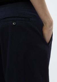 Marineblauwe broek van katoen, met een achterzak met knoopsluiting en subtiele textuurdetails langs de tailleband.