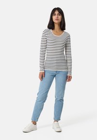 Maglia a maniche lunghe a righe in crema e blu navy, con scollatura rotonda, abbinata a jeans azzurri chiari e sneakers bianche.