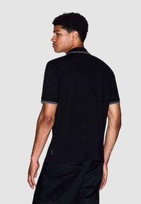 Zwarte poloshirt met grijze accenten bij de kraag en mouwen, met een klassieke fit en een zachte textuur, gedragen met bijpassende zwarte shorts.
