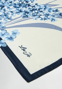 Silketørklæde med et blåt blomstermotiv på en cremefarvet baggrund, med en marineblå kant og "Liu Jo" signatur. Blød tekstur, rektangulær form.