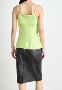 Grüne Satin-Camisole mit verstellbaren Trägern, kombiniert mit einem schwarzen Leder-Bleistiftrock mit seitlichem Reißverschluss und gesteppten Nähten.
