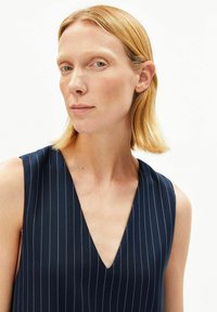 Marineblauwe mouwloze top met een V-hals ontwerp, voorzien van dunne verticale witte strepen, een gladde stoffen textuur en een getailleerde pasvorm.