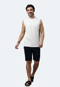 Weißes ärmelloses Shirt, dunkle Shorts und schwarze Sandalen. Baumwolltextur, lässiges Design. Silhouette zeigt eine gehende männliche Figur.