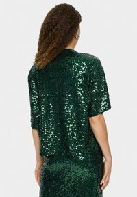 Haut à paillettes vert avec une coupe ample et des manches courtes. La texture scintillante crée une apparence brillante, conçu avec un col rond.