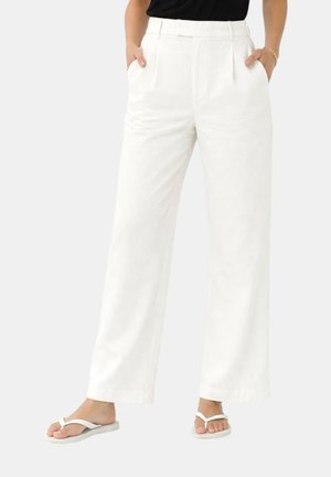 Donna che indossa pantaloni bianchi a vita alta e gamba larga con pieghe frontali e tasche laterali, abbinati a sandali bianchi infradito e top nero.