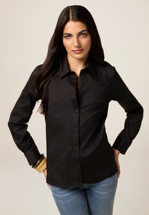 Black long-sleeve button-up shirt with a classic collar, featuring a smooth texture and fitted design, paired with blue jeans and bracelets.