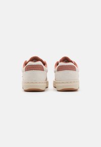 Białe zamszowe trampki z rdzawymi akcentami, teksturowany materiał na kołnierzu kostki oraz beżowe gumowe podeszwy. Nazwa marki wytłoczona na pięcie.