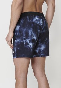 Vyriški maudymosi šortai tamsiai mėlynos spalvos su tie-dye raštu, elastinga juosmens juosta ir šoninėmis kišenėmis. Lengvas ir glotnus audinys.