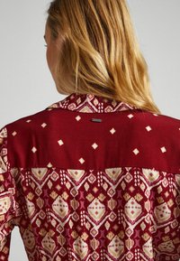 Chemise à motifs rouges avec une partie inférieure à motifs comprenant des diamants et des formes géométriques, et une section supérieure unie avec col.