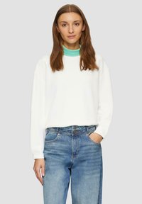 Sudadera blanca con cuello verde menta, de corte relajado y mangas largas, combinada con jeans de denim de lavado claro.
