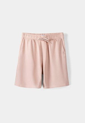 Jasnoróżowe, casualowe szorty z elastycznym paskiem, sznurkiem z przodu i bocznymi kieszeniami, prezentowane na jednolitym białym tle.