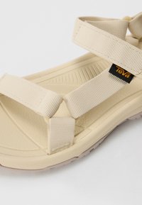 Beige sandaalit, joissa on teksturoitu kumipohja, säädettävät remmit ja logotagi. Ominaisuuksiin kuuluu pehmustettu pohja, joka tarjoaa mukavuutta ja pitoa.
