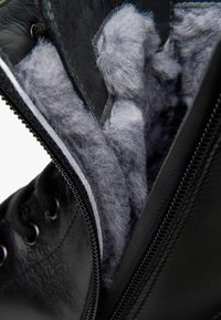 Schwarzer Lederstiefel mit einem Reißverschluss, ausgestattet mit einem grauen, weichen Futter, das Wärme und Komfort bietet. Texturierte Außenseite und robustes Zubehör.