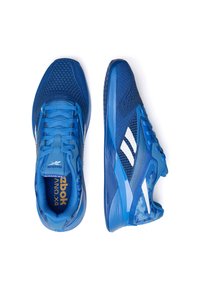 Zili zili sporta apavi ar acs audumu augšdaļu, baltām akcentiem, teksturētām zolēm un izteiktu Reebok logotipu. Ievērojama plūstoša forma un šņorējums.