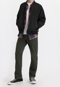 Svart bomberjacka, vit T-shirt, flanellskjorta i blått och rött, olivgröna byxor, svarta sneakers med vit sula.