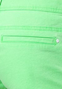 Gros plan d’un tissu vert vif avec une poche arrière horizontale dotée d’un bouton blanc sur le côté droit.