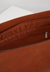 Interior de bolso de cuero marrón con una textura suave y lisa, y un bolsillo con cremallera que tiene una lengüeta de tirador plateada. El forro es de tela marrón a juego.