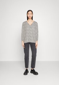 Langermet, V-hals bluse i beige med svart abstrakt mønster; kombinert med mørkegrå smale jeans og svarte snørestøvler.