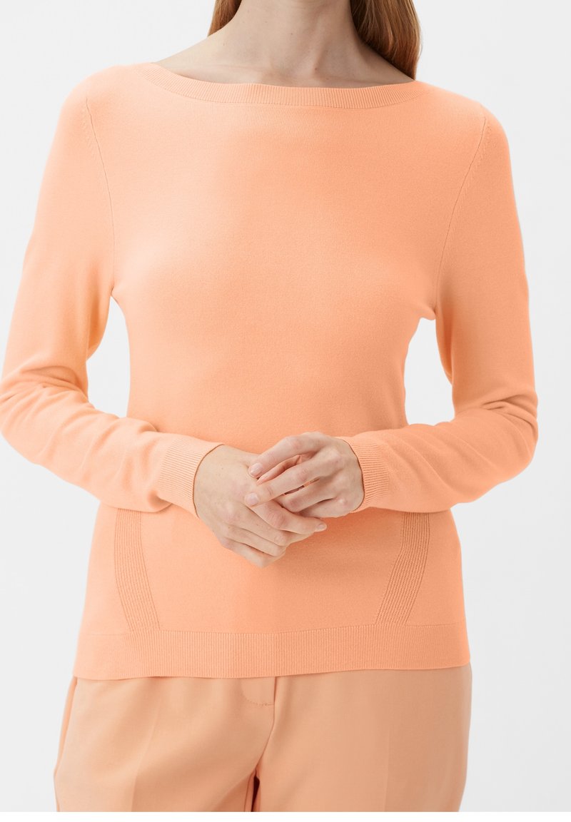 Pull tricoté orange clair à manches longues et encolure bateau. Présente des accents texturés sur les côtés et des poignets côtelés.