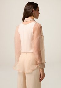 Doorzichtige perzikkleurige blouse met een kraag, lange mouwen en knoopmanchetten. Gelaagd ontwerp met een gladde, lichte textuur.