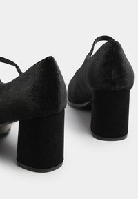 Scarpe con tacco alto in velluto nero, con punta tonda e tacco a blocco spesso. Presentano una delicata fascia alla caviglia. Tessuto testurizzato.