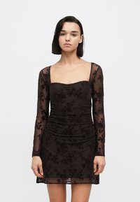 Schwarzes, gerafftes Bodycon-Kleid mit langen transparenten Ärmeln, verziert mit floraler Spitzenbesatz und eckigem Ausschnitt. Glatte Textur mit figurbetonter Silhouette.