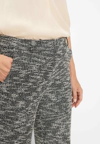 Textuur zwaar zwart-wit geometrisch patroon met een hoge tailleband, twee opgestikte zakken aan de voorkant en een relaxte pasvorm. Extra detail zichtbaar bij de tailleband.