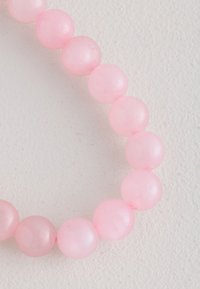 Rosa-rosafarbenes Perlenarmband mit glatten, runden Perlen von gleichmäßiger Größe und leicht durchscheinendem Finish vor hellem Hintergrund.