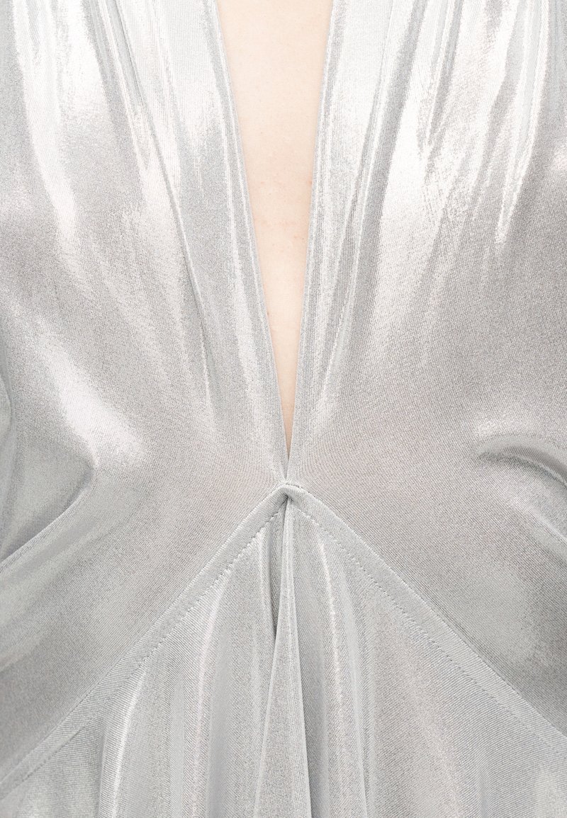 Gros plan sur un tissu métallique argenté formant un profond décolleté en V avec des fronces au centre devant.