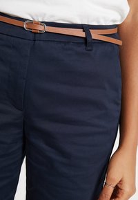 Pantalons navy avec une ceinture en cuir marron dotée d'une boucle en argent. Texture lisse et coupe ajustée. Passants de ceinture visibles sur la taille.
